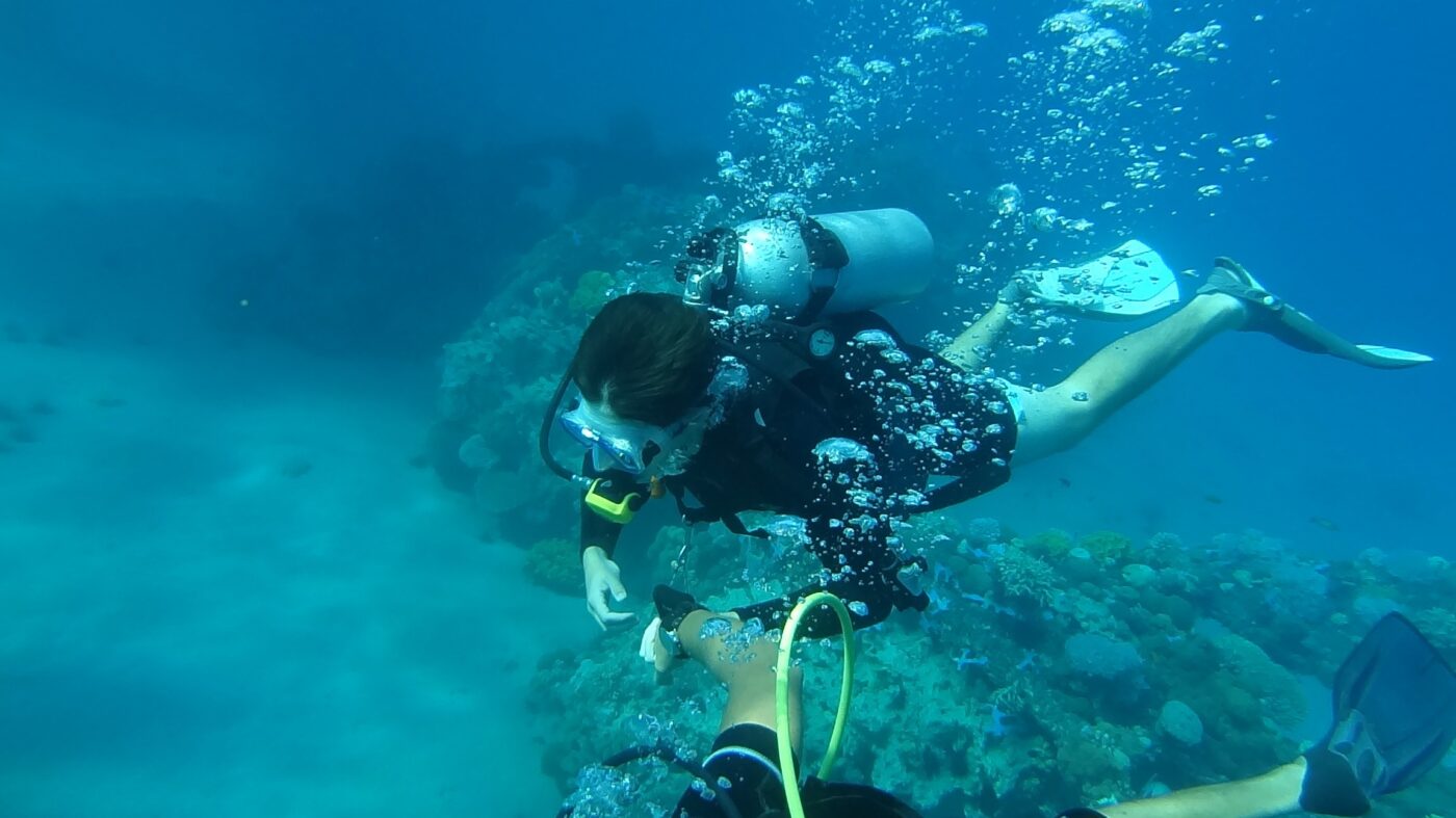 scuba diver underwater exploring coral reef with air tank and bubbles in deep blue ocean